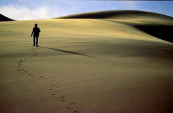 A imagem mostra um homem atravessando um deserto